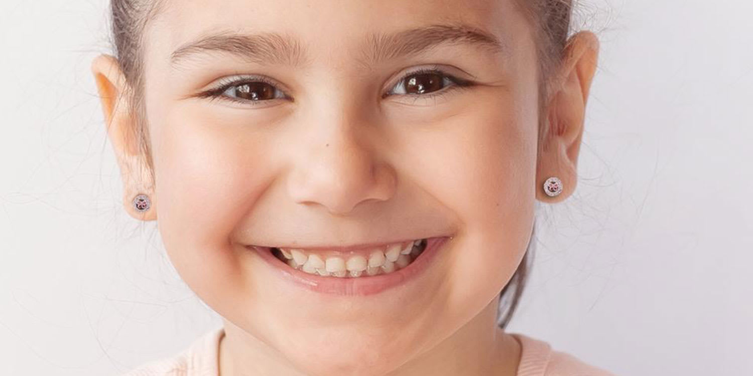 Lächelndes Mädchen trägt kleine Ohrstecker mit Kristallsteinen