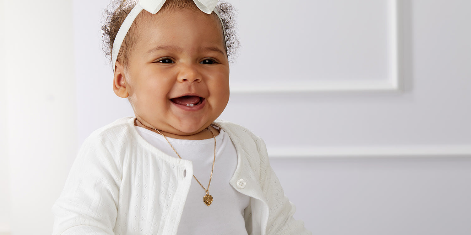 Lächelndes Baby mit weißem Haarband trägt zarte goldene Halskette mit rundem Anhänger