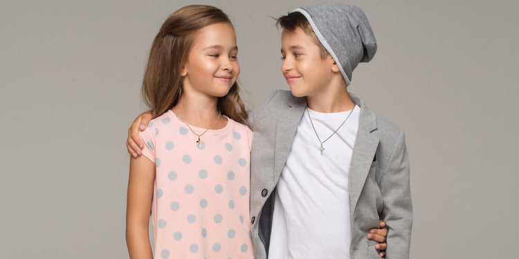 Lächelnde Geschwister umarmen sich - Mädchen trägt Kreuz-Halskette, Junge trägt silberne Halskette