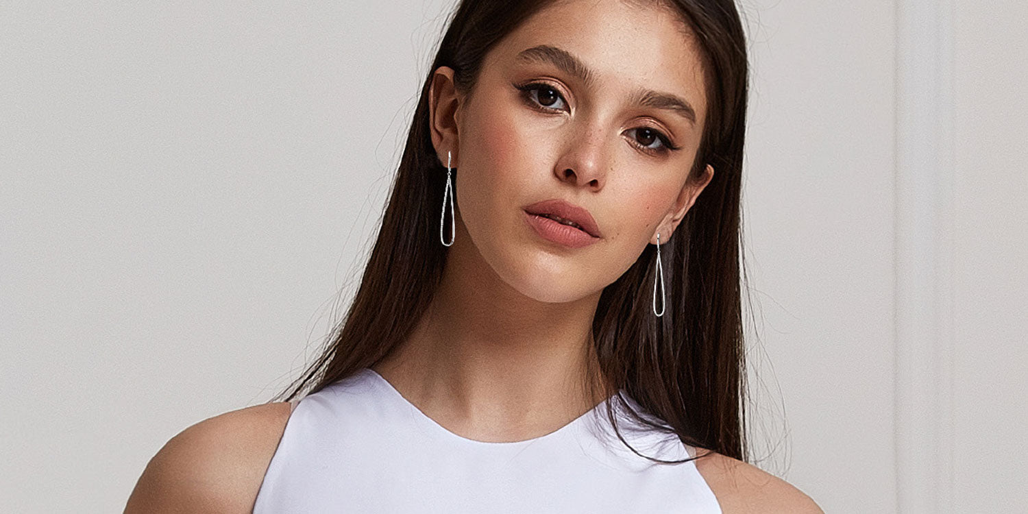 Junge Frau mit langen dunklen Haaren trägt elegante silberne Diamant-Ohrringe und ein weißes ärmelloses Top