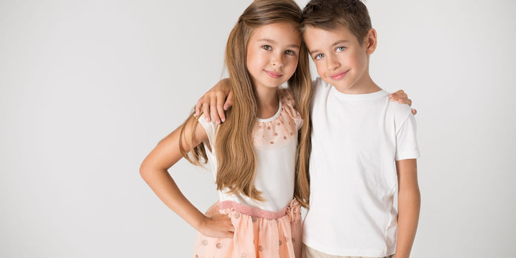 Zwei lächelnde Kinder umarmen sich - Mädchen mit langen blonden Haaren trägt rosa Kleid, Junge trägt weißes T-Shirt - Kinderschmuck