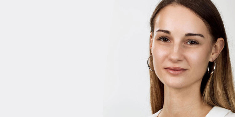 Frau mit glatten brünetten Haaren trägt silberne Creolen-Ohrringe und ein weißes Oberteil, lächelnd vor hellem Hintergrund