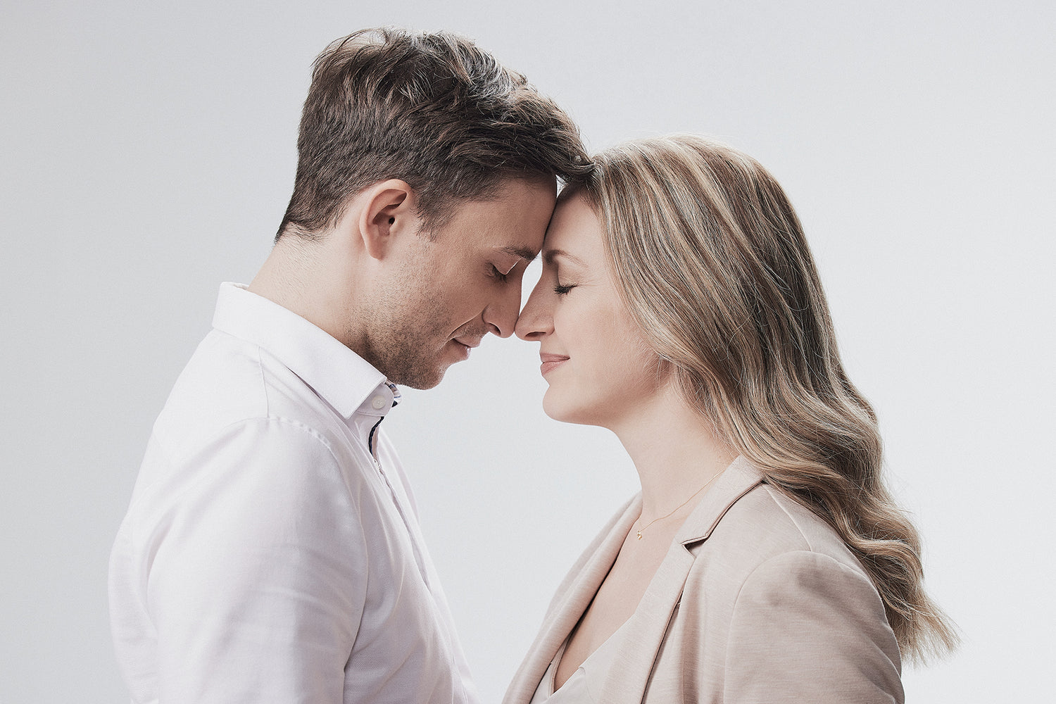 Romantisches Paar in zarten Farbtönen - Mann in weißem Hemd, Frau in beigem Blazer mit zartem Schmuck