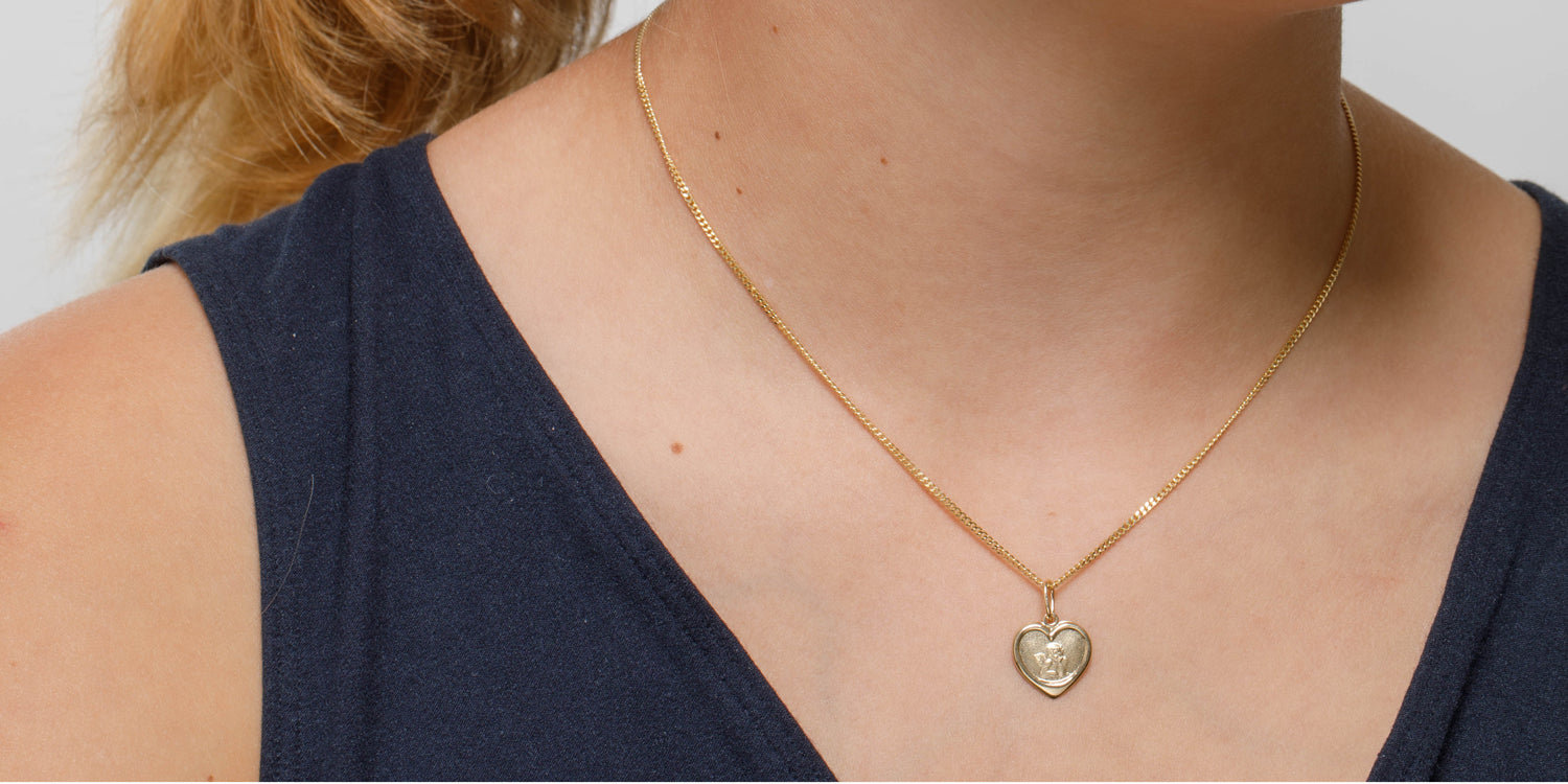 Goldene Halskette mit herzförmigem Schutzengel-Anhänger am Dekolleté getragen