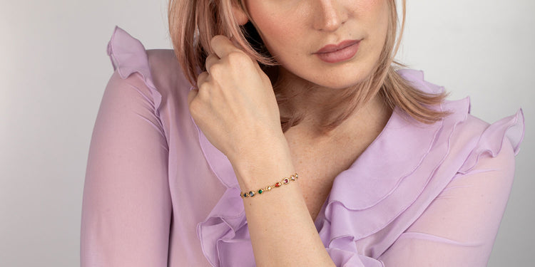 Frau in lila Rüschenbluse trägt goldenes Armband mit bunten Edelsteinen am Handgelenk