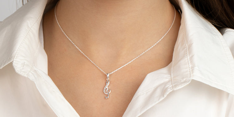 Silberne Halskette mit Notenschlüssel-Anhänger am Dekolleté getragen