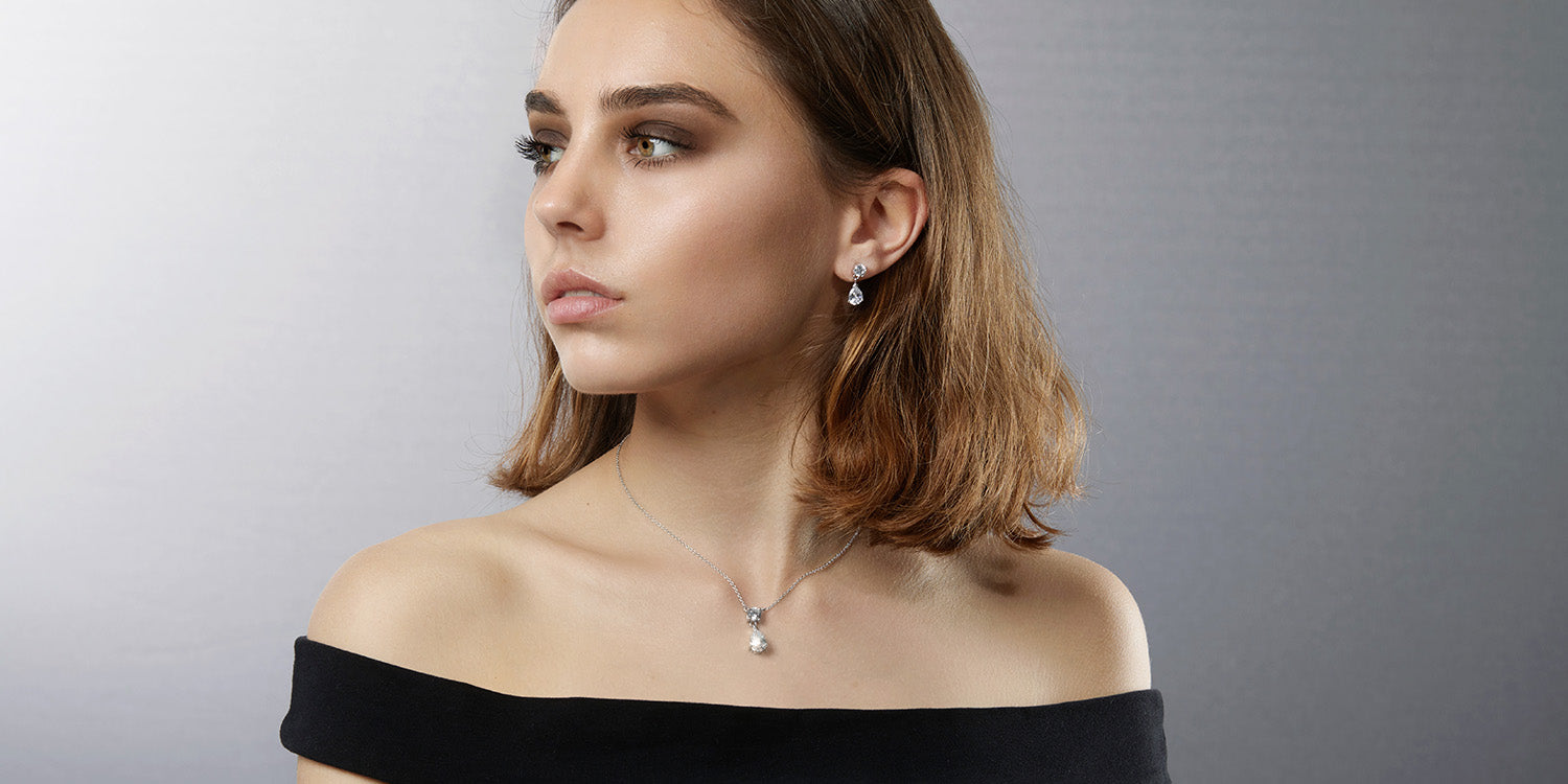 Frau mit schulterlangem braunem Haar trägt elegante Perlen-Ohrringe und eine zarte Perlenkette zu einem schwarzen schulterfreien Top