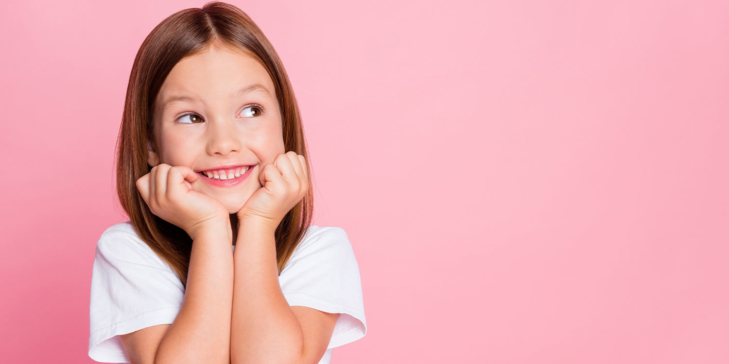 Lächelndes Mädchen trägt bunte Kinderringe an beiden Händen vor rosa Hintergrund